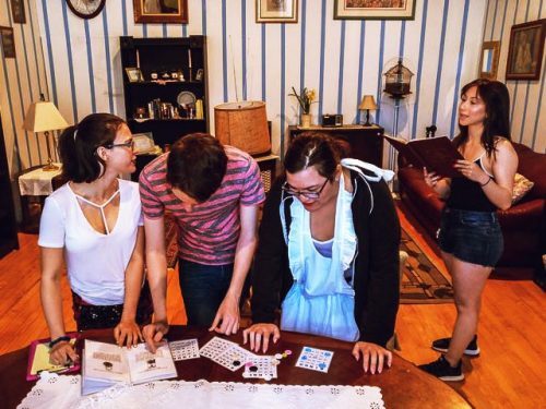 Three People Looking At Puzzles On A Table While Another Holds A Book